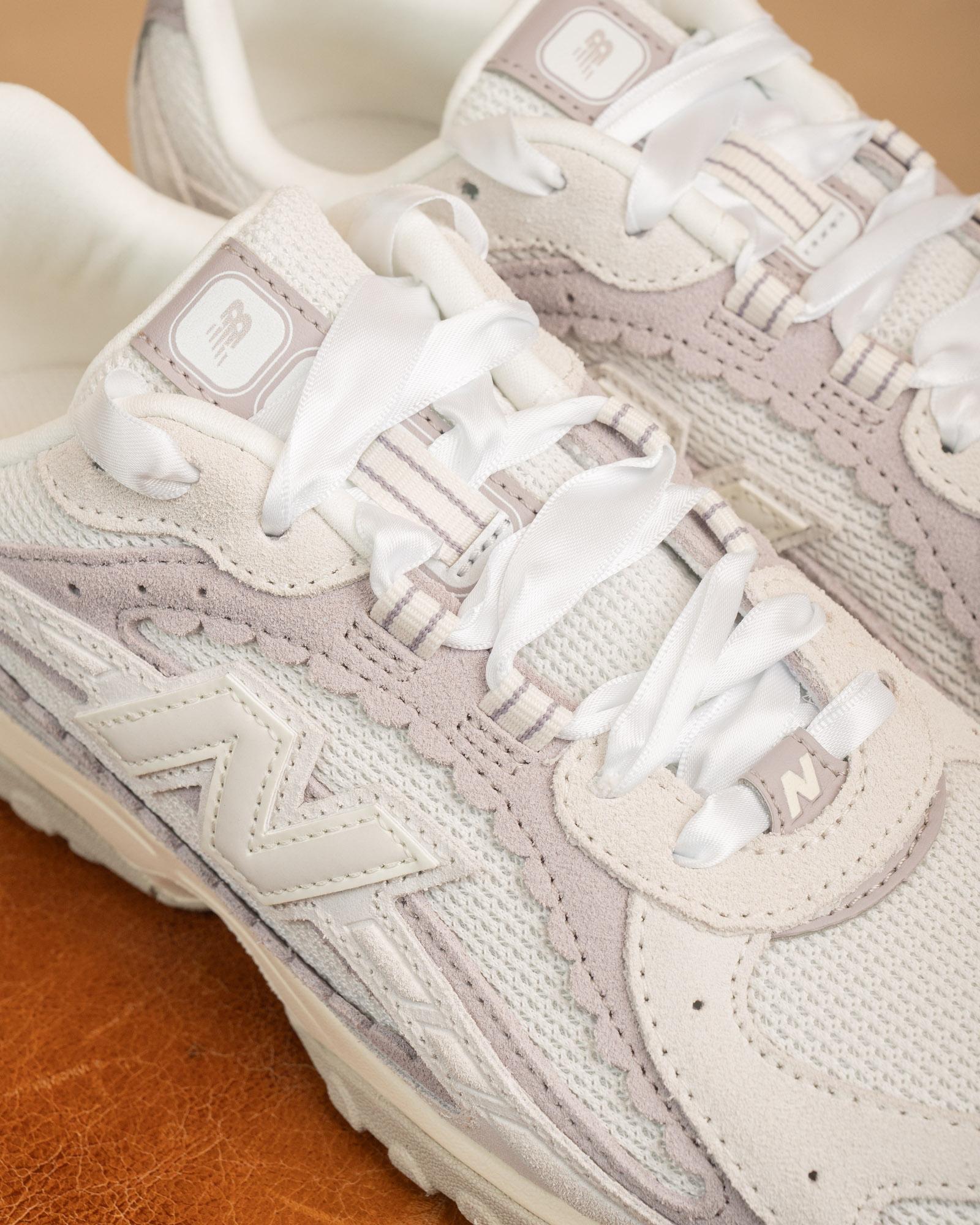 Primo piano delle New Balance 204 bianche e lilla, scarpa stringata dal design minimalista con tomaia in pelle premium.