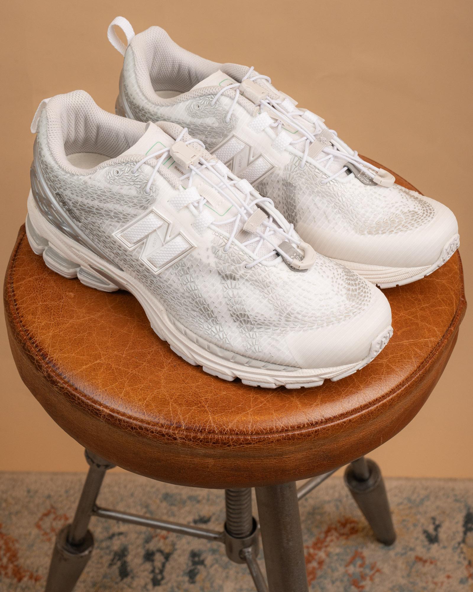 Sneakers New Balance 1906R in mesh bianco con sovrapposizioni sintetiche argento metallizzato e dettagli grigio chiaro.